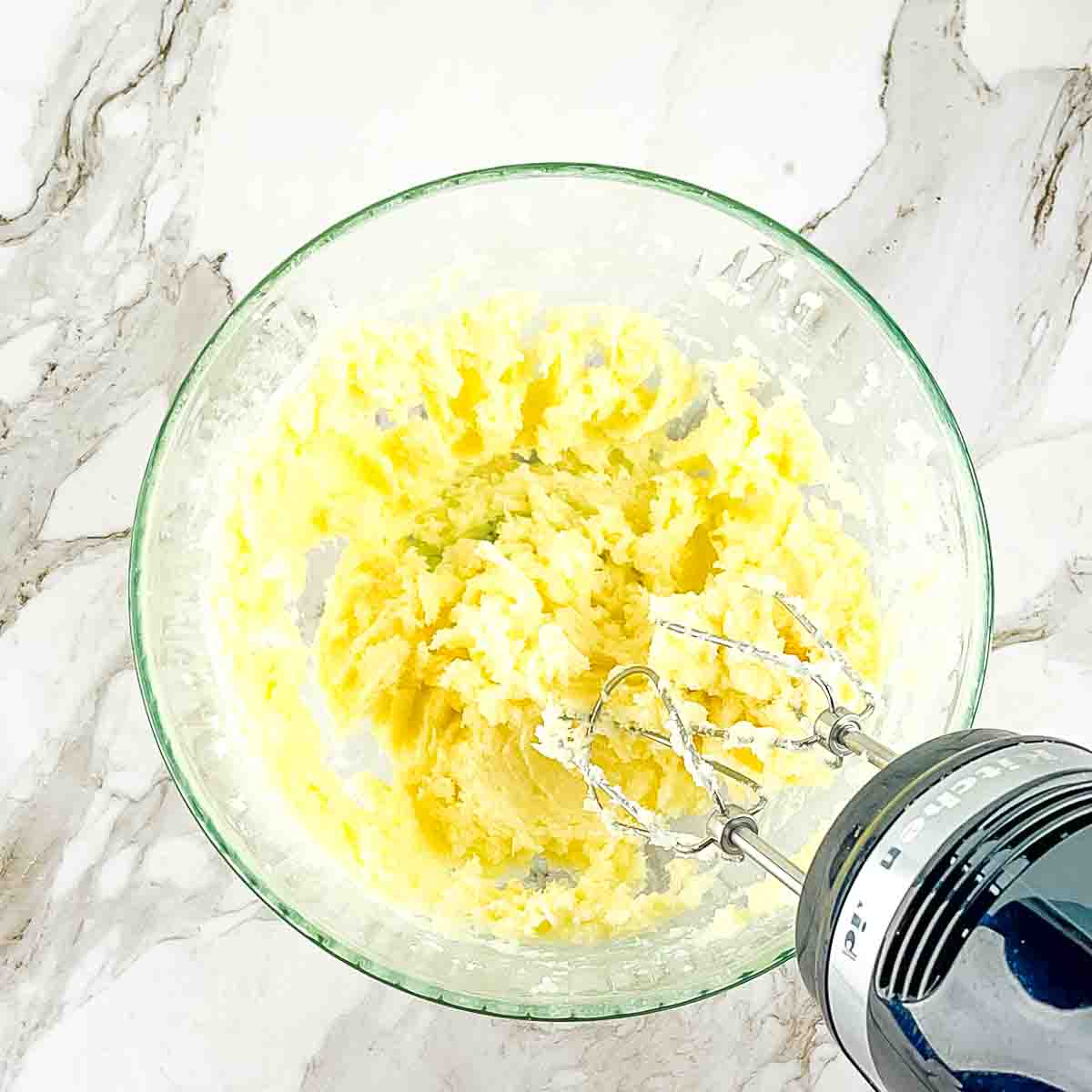 An electric mixer combining the butter and sugar in a bowl until creamy.