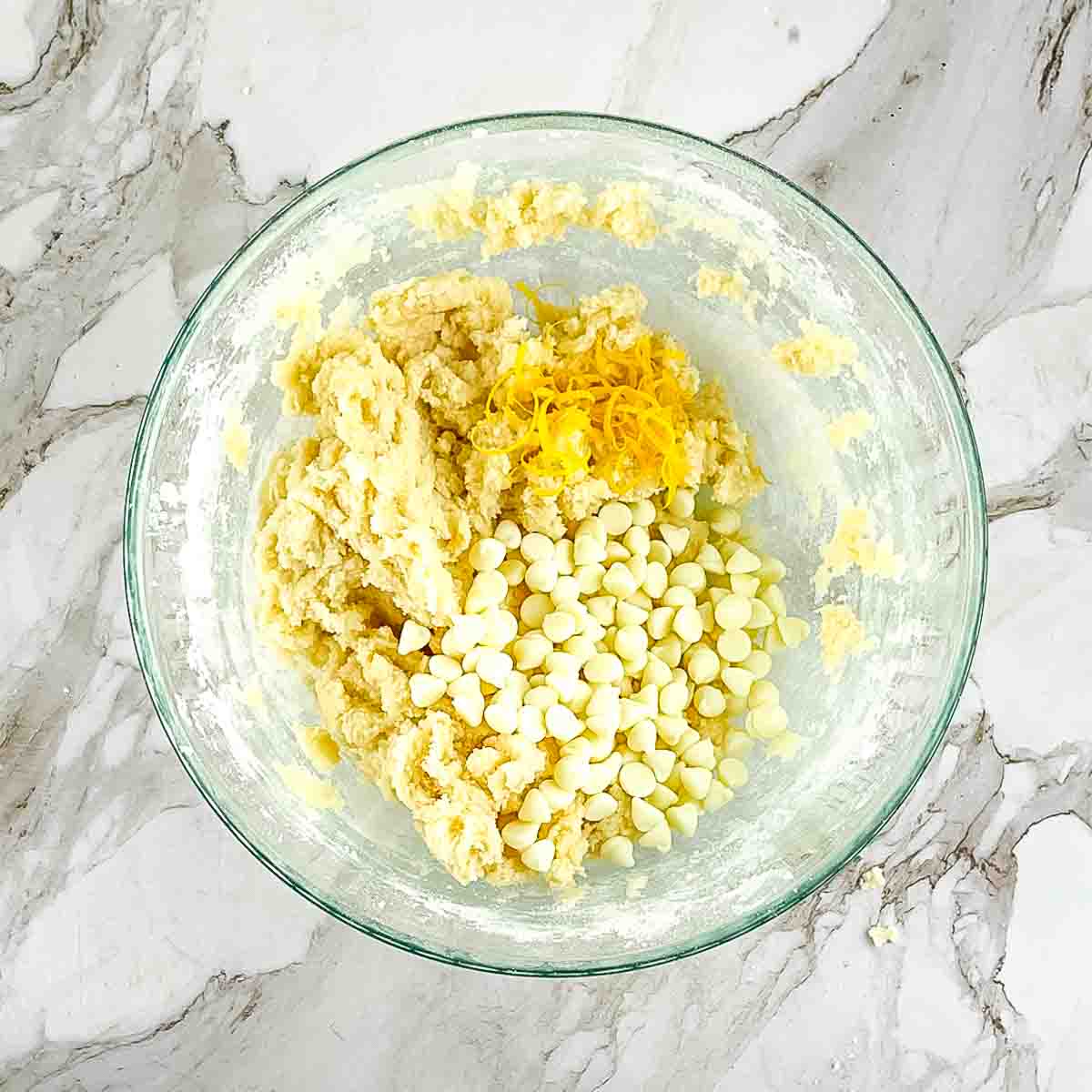 The ingredients combined in a glass mixing bowl, with the lemon zest and white chocolate chips added.