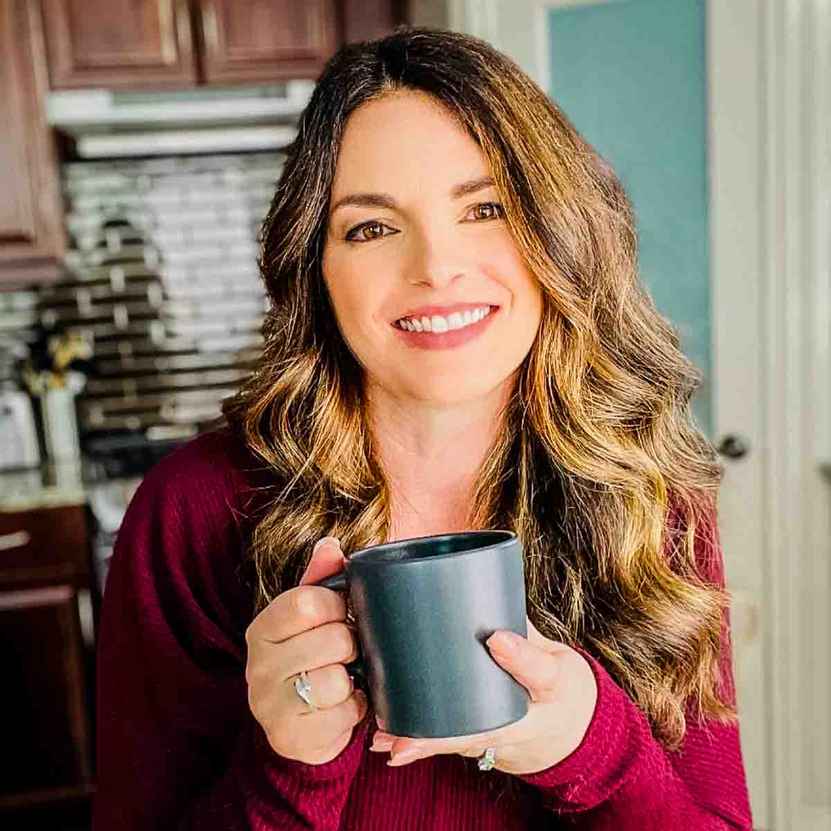 A photo of Jeri Walker smiling in her kitchen while holding a cup of coffee, welcoming her readers to her website.