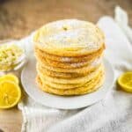 A stack of lemon drop cookies on a white plate, dusted with powdered sugar.