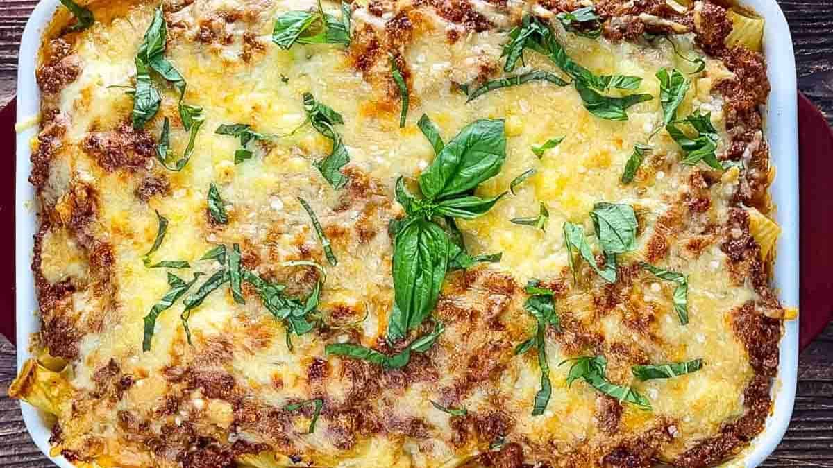 A casserole dish of Rigatoni al Forno topped with melted cheese and fresh basil.