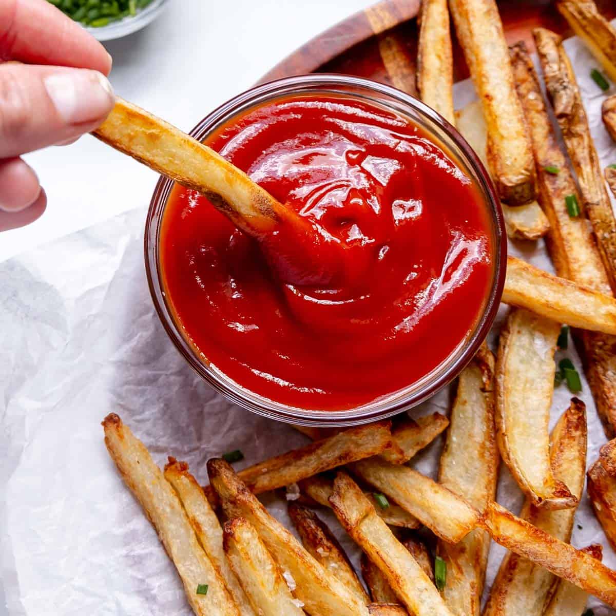 A hand dipping a french fry in ketchup.