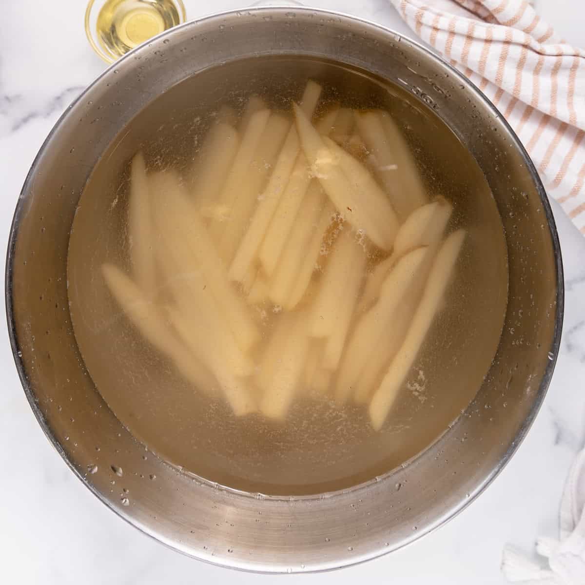 A metal bowl holding french fries soaked in water.
