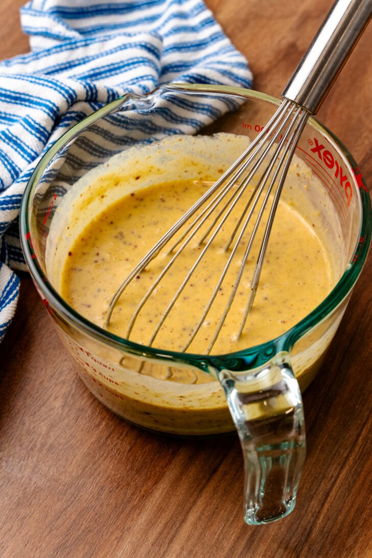 Honey mustard in a mixing bowl with a wire whisk.