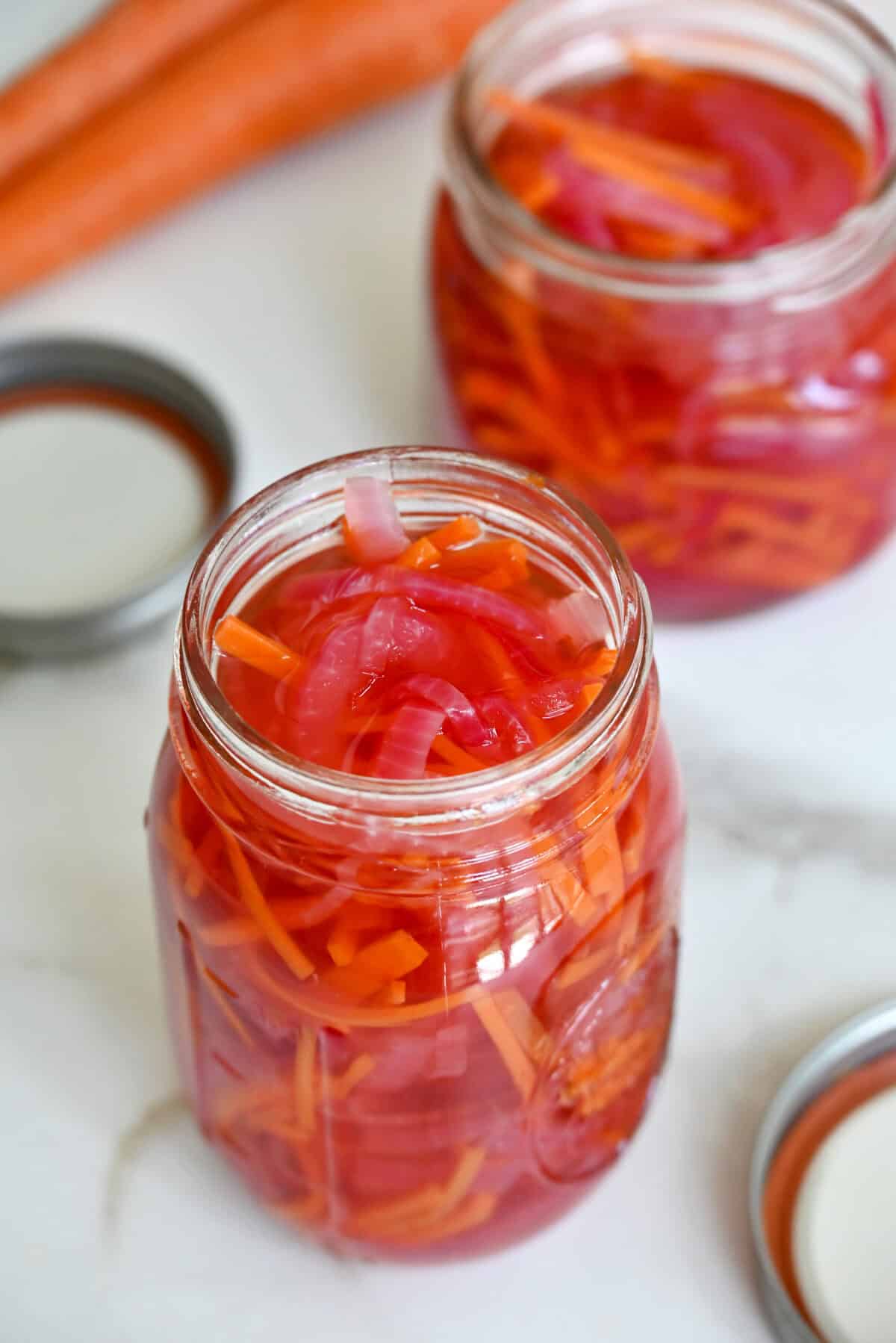 Two mason jars filled with pickled red onions and carrots.